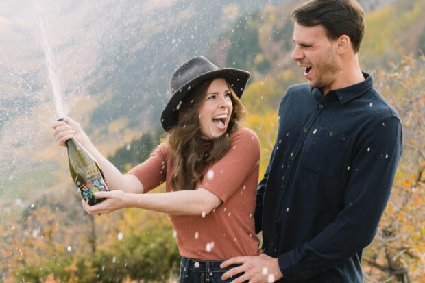 engaged couple popping champagne in Colorado mountains
