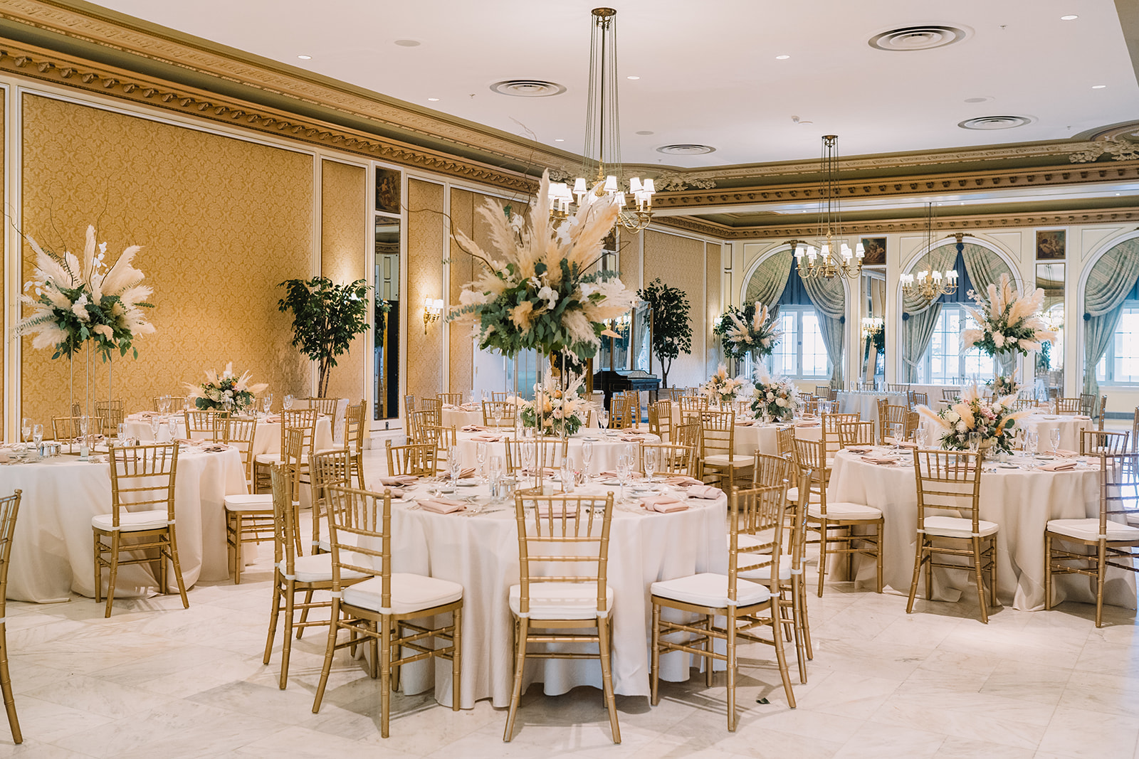 wedding reception room photo with golden chairs and pampas grass floral decor