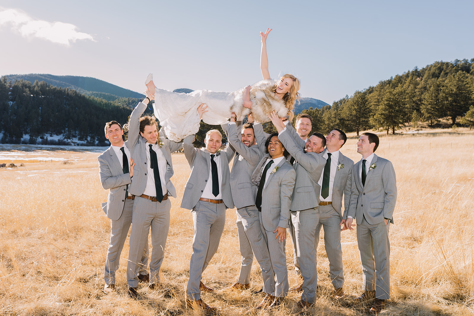 groomsmen holding up the bride with big smiles on everyone's faces in a beautiful valley with a mountain in the background